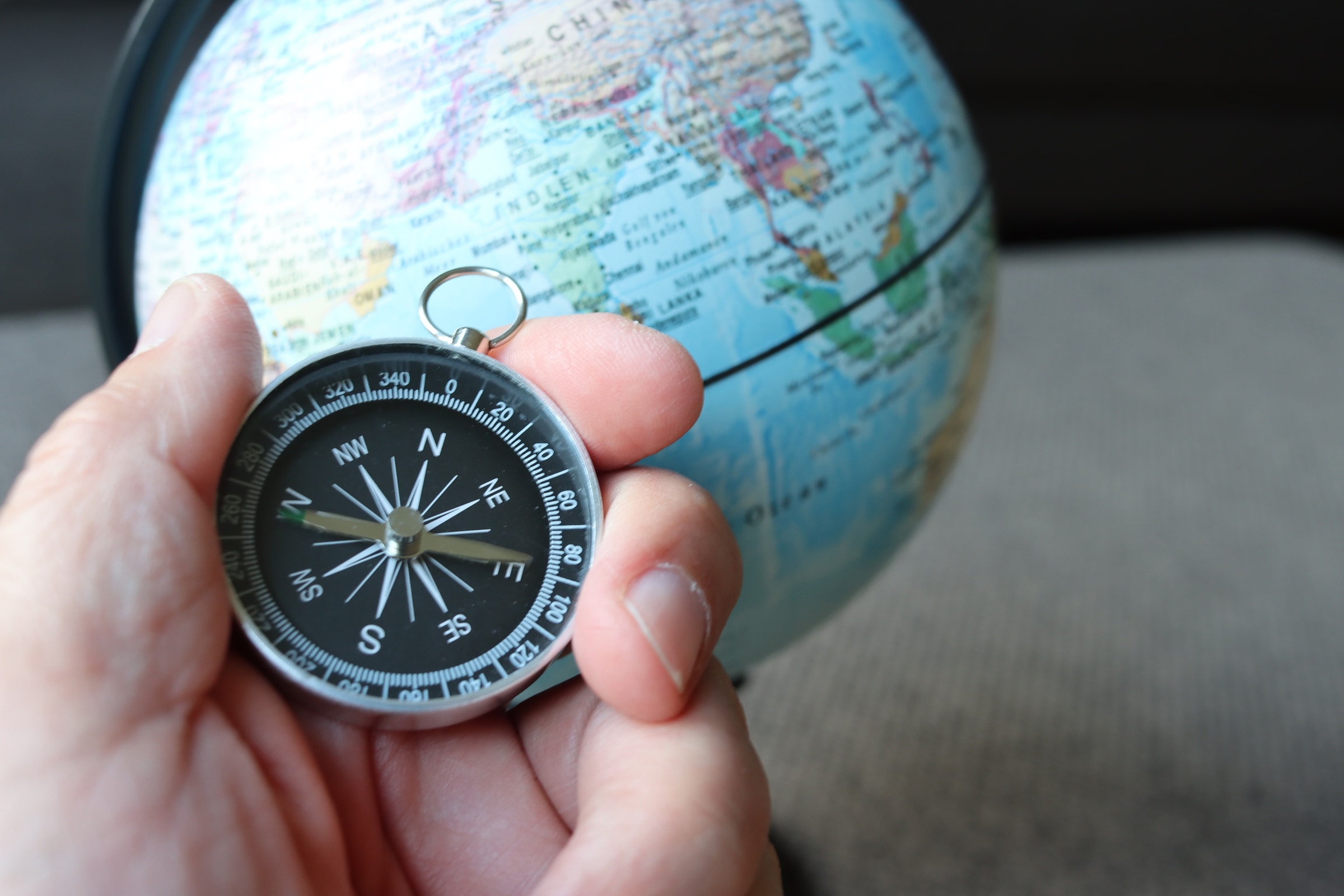 A hand holding a compass in front of a globe, symbolizing travel and navigation.