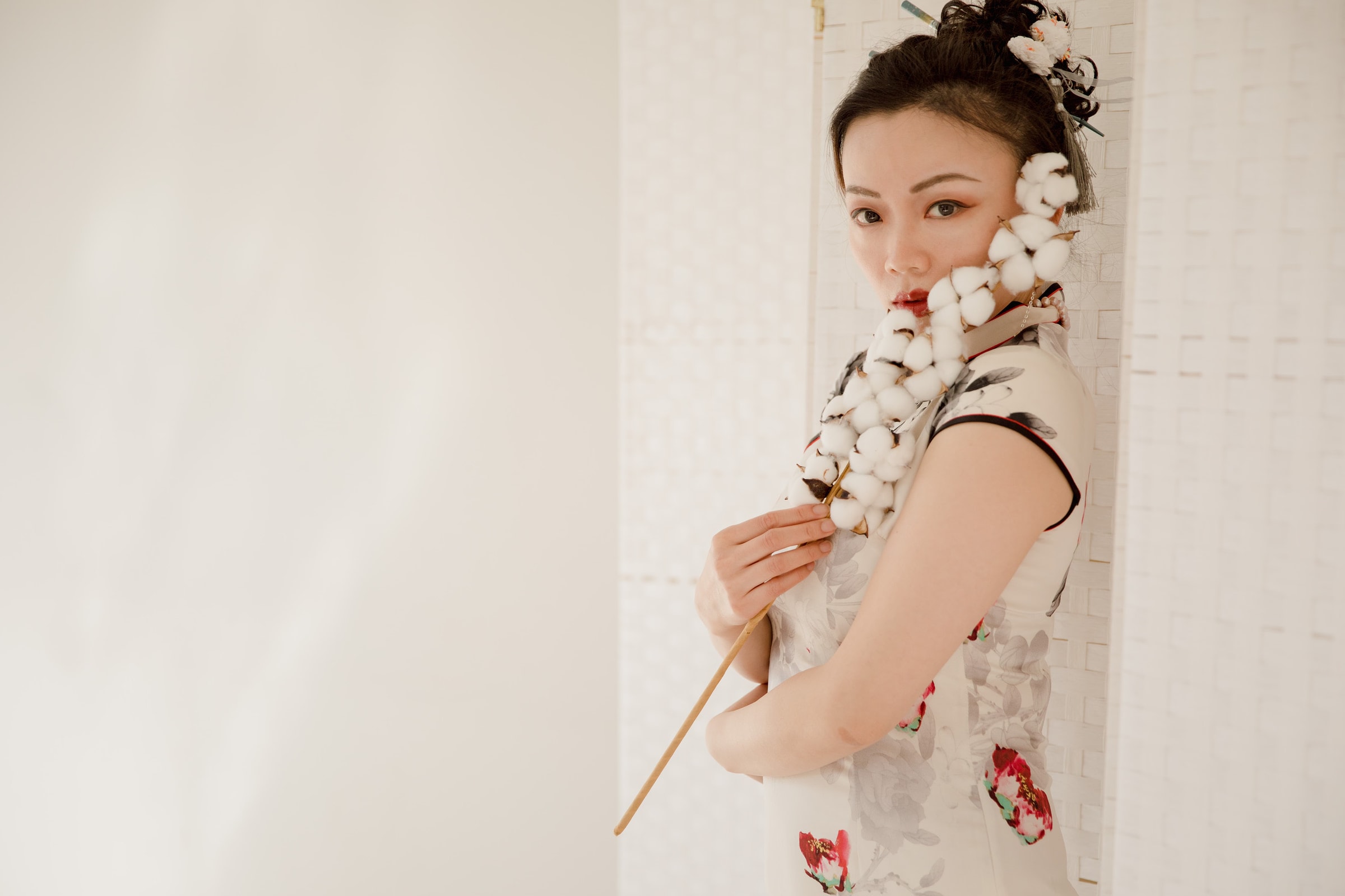 Portrait of a woman in a floral qipao holding cotton, showcasing traditional style.